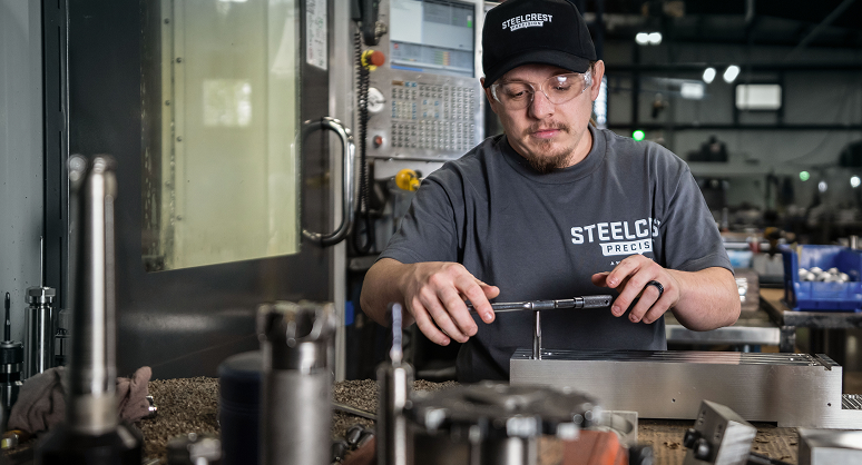 A Steelcrest Precision expert working on tools and equipment in a machine shop setting